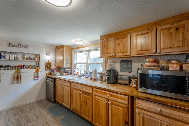 kitchen featuring wooden counters, baseboards, appliances with stainless steel finishes, a textured ceiling, and a sink