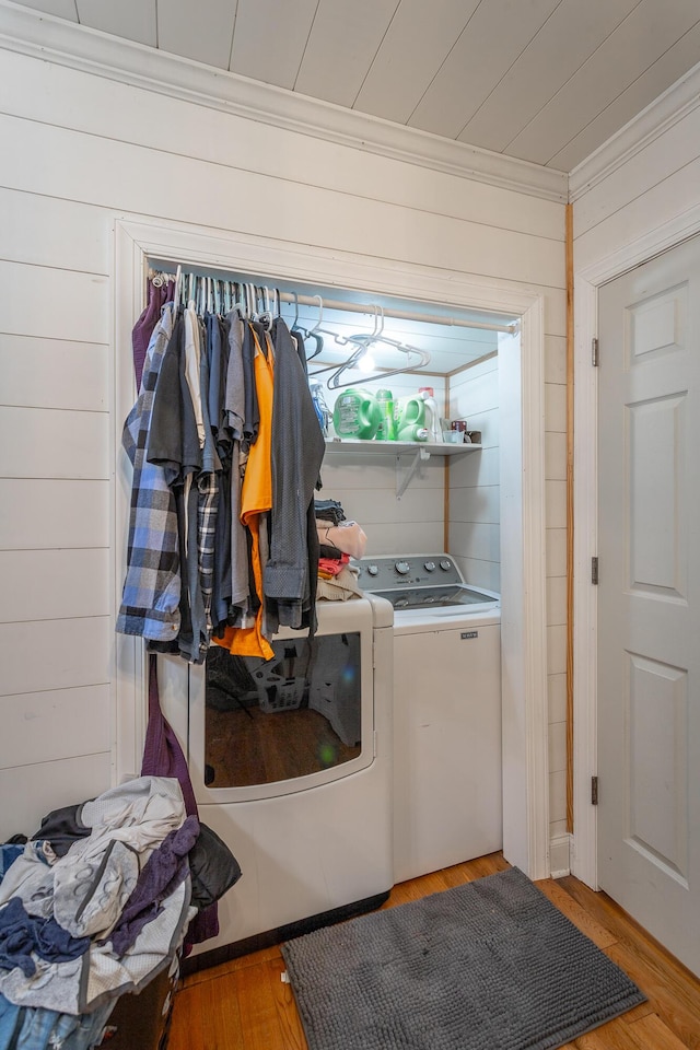 laundry room featuring washer and clothes dryer, wood walls, crown molding, and light wood-type flooring