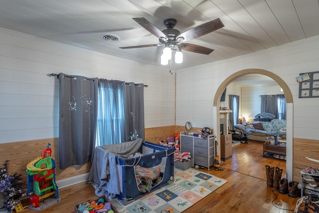 rec room with hardwood / wood-style floors, a ceiling fan, visible vents, arched walkways, and crown molding