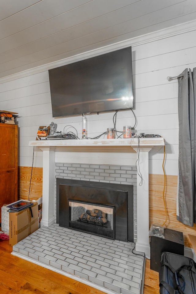 room details featuring crown molding, wood finished floors, a fireplace, and wood walls