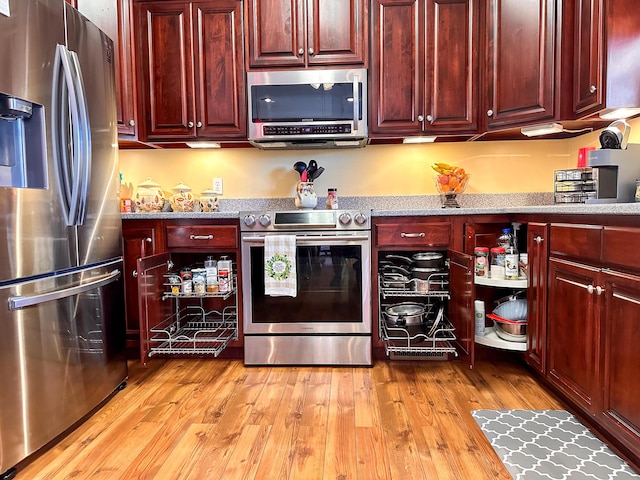 kitchen featuring light wood-style flooring, light stone countertops, appliances with stainless steel finishes, and reddish brown cabinets