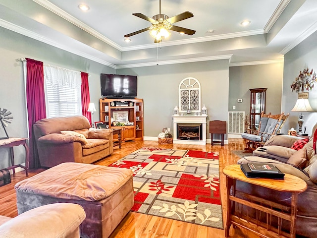 living room featuring visible vents, a fireplace with raised hearth, crown molding, a tray ceiling, and wood finished floors