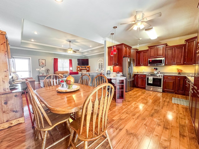 dining space featuring a raised ceiling, light wood-style floors, ceiling fan, and ornamental molding