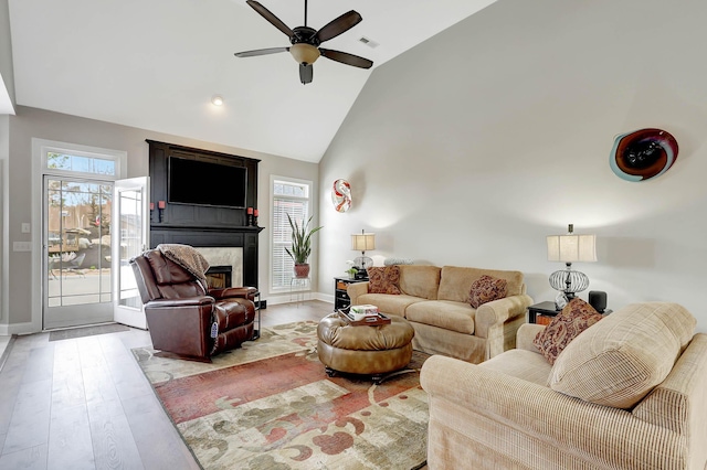 living area with wood finished floors, baseboards, visible vents, a premium fireplace, and high vaulted ceiling