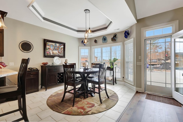 dining space with visible vents, light wood-type flooring, a raised ceiling, and ornamental molding