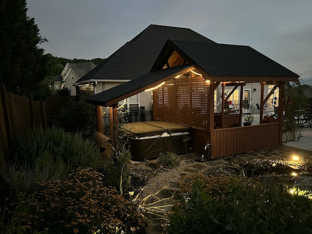 view of home's exterior with a wooden deck, a hot tub, a shingled roof, and fence