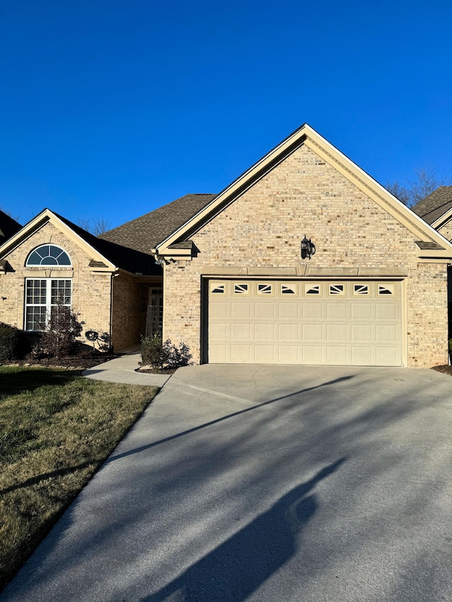 ranch-style home featuring brick siding, concrete driveway, an attached garage, and a shingled roof