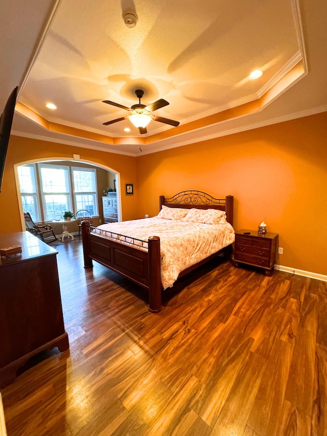 bedroom with baseboards, a tray ceiling, ornamental molding, dark wood-style floors, and arched walkways