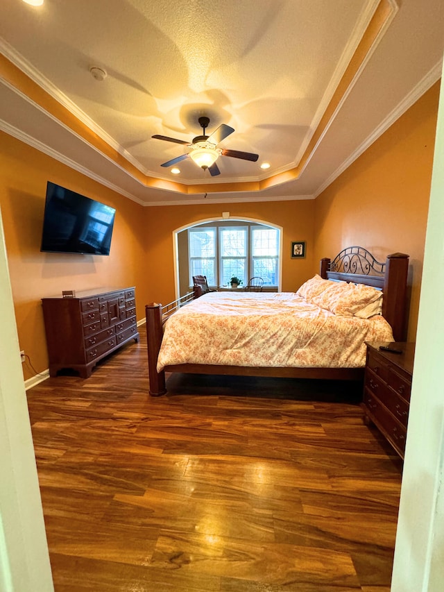 bedroom featuring wood finished floors, baseboards, a tray ceiling, ornamental molding, and a textured ceiling