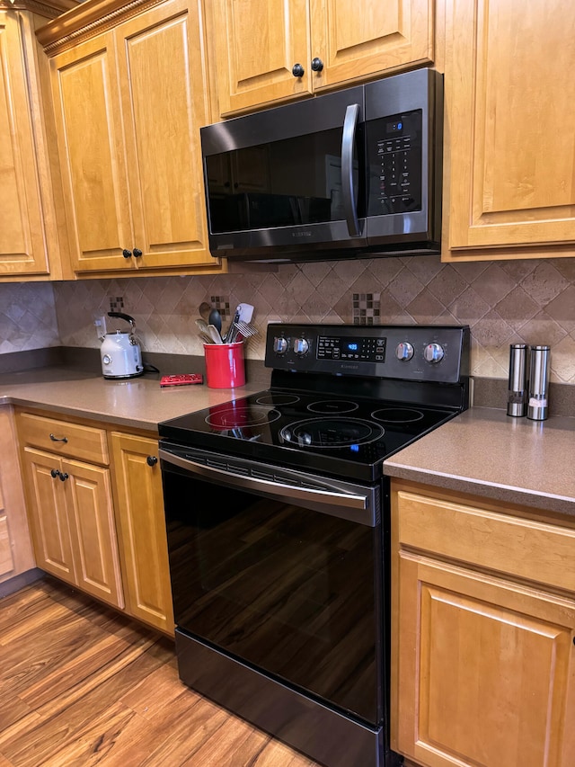 kitchen featuring decorative backsplash, black range with electric stovetop, and wood finished floors