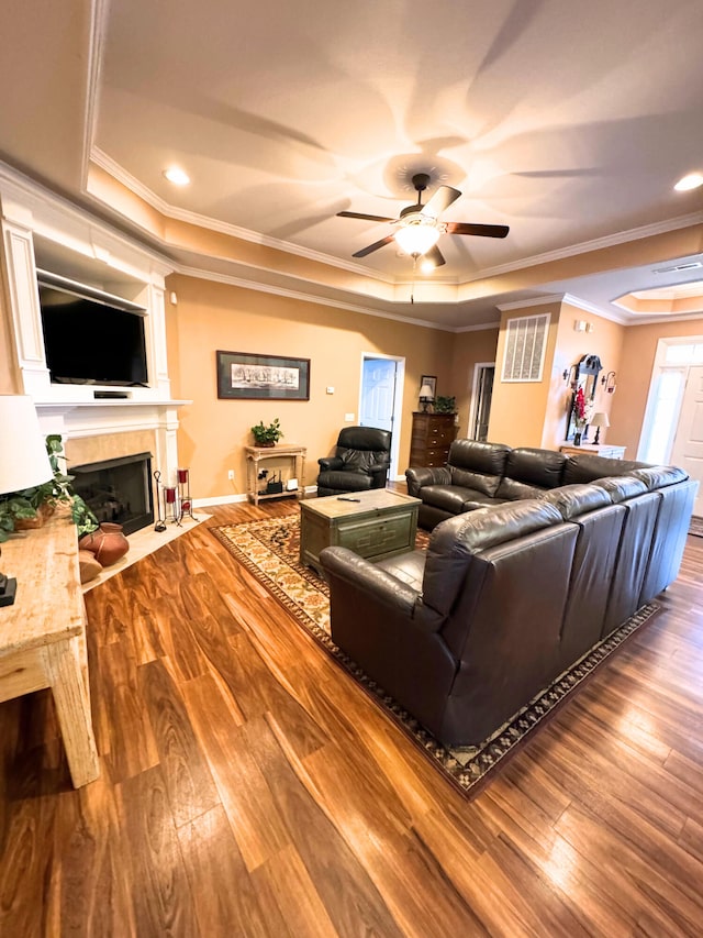 living room with a tray ceiling, wood finished floors, and crown molding