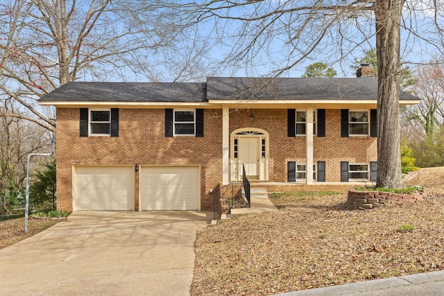 raised ranch with driveway, a shingled roof, a garage, brick siding, and a chimney