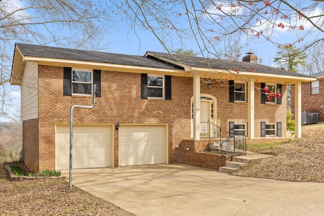 split foyer home featuring concrete driveway, a garage, brick siding, and a chimney