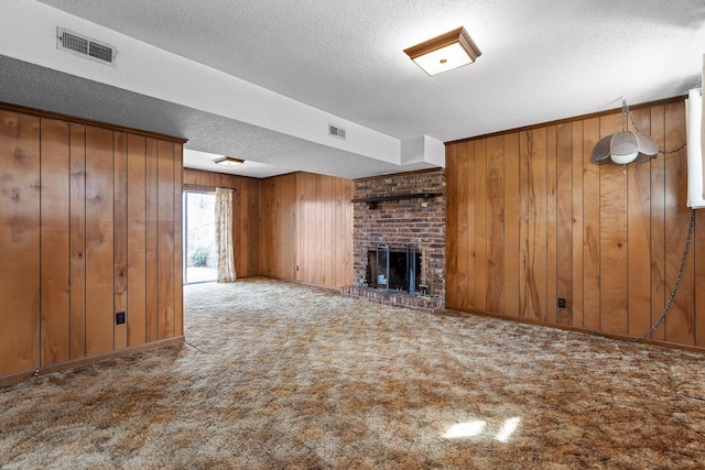 unfurnished living room featuring a brick fireplace, wooden walls, carpet, and visible vents