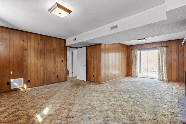 carpeted spare room with wooden walls, visible vents, and a textured ceiling