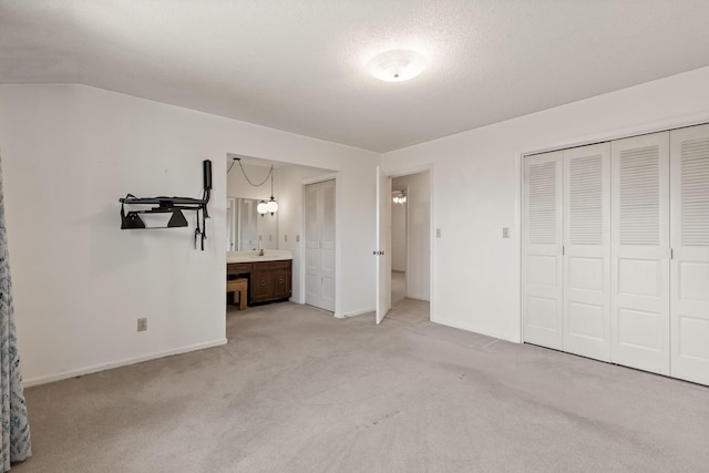 unfurnished bedroom featuring light carpet, connected bathroom, a textured ceiling, and baseboards