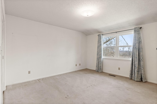 empty room with visible vents, baseboards, light colored carpet, lofted ceiling, and a textured ceiling