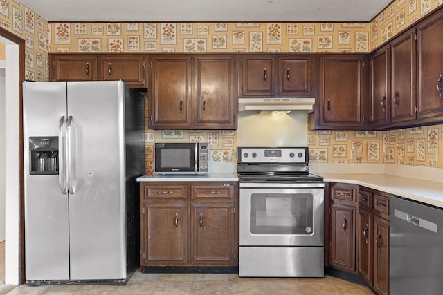 kitchen with under cabinet range hood, stainless steel appliances, light countertops, and wallpapered walls