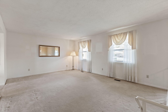 empty room with visible vents, carpet flooring, a textured ceiling, and baseboards