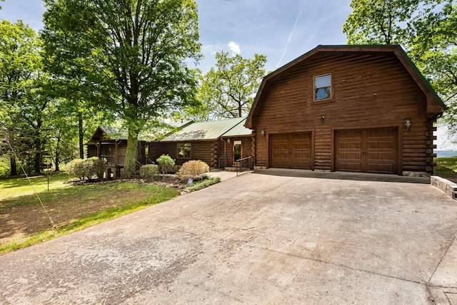 view of front facade with a gambrel roof, concrete driveway, log siding, metal roof, and a garage