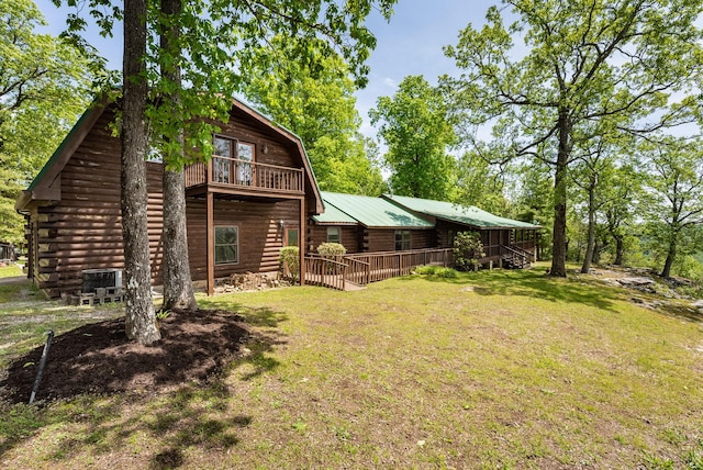 back of property featuring log siding, central AC unit, metal roof, a balcony, and a yard