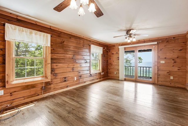 unfurnished room with wooden walls, a healthy amount of sunlight, a ceiling fan, and wood finished floors