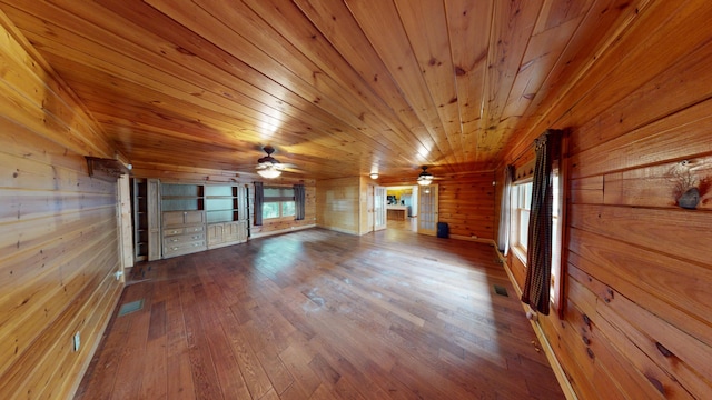 unfurnished living room with visible vents, wood-type flooring, wood walls, wooden ceiling, and ceiling fan