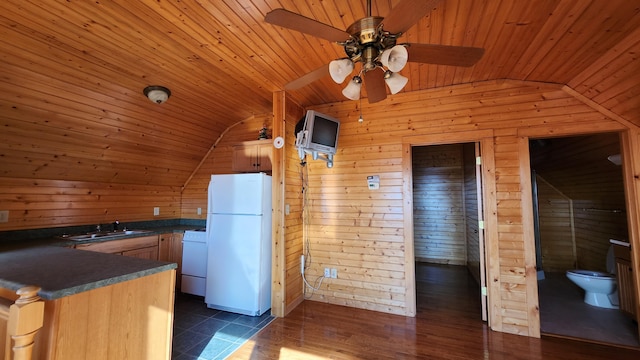 kitchen featuring wooden walls, lofted ceiling, freestanding refrigerator, a sink, and dark countertops