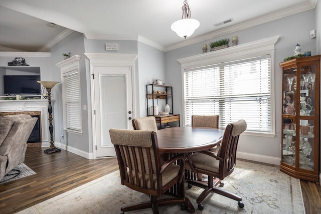 dining space featuring visible vents, crown molding, baseboards, a fireplace, and wood finished floors