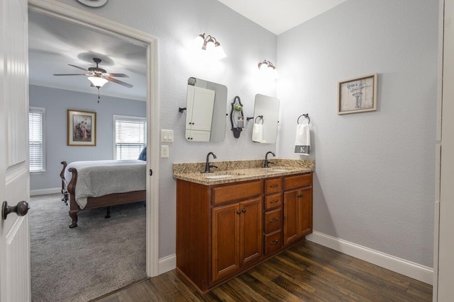 ensuite bathroom featuring double vanity, wood finished floors, baseboards, and a sink