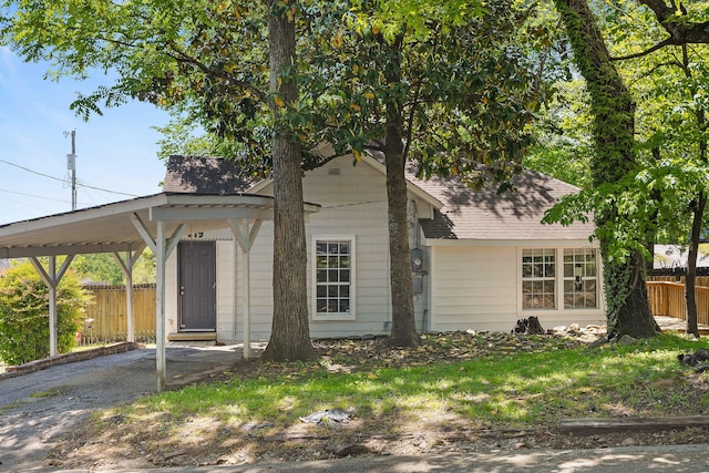 view of front facade with a carport, driveway, roof with shingles, and fence