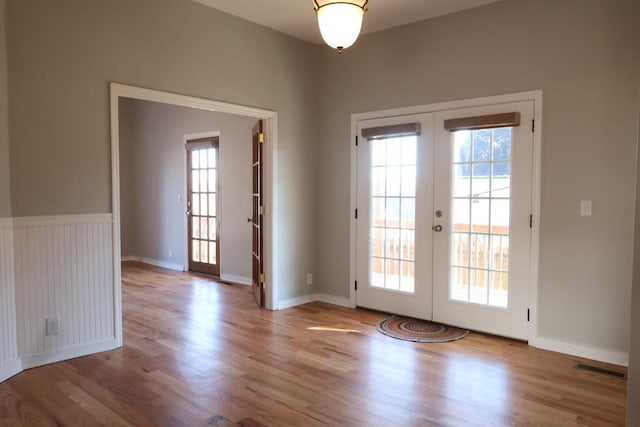 doorway with a wainscoted wall, wood finished floors, french doors, and visible vents