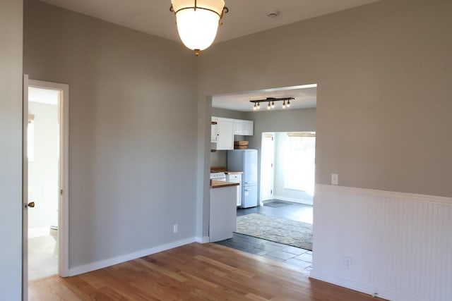 unfurnished dining area with track lighting, wainscoting, baseboards, and wood finished floors