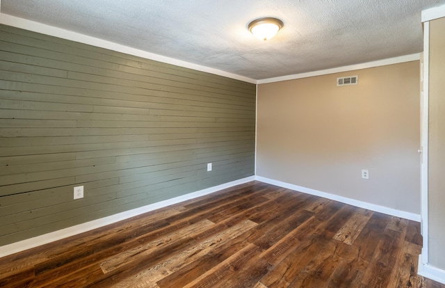 spare room with baseboards, visible vents, dark wood finished floors, wood walls, and a textured ceiling