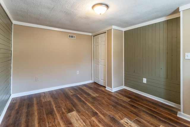 unfurnished bedroom with dark wood-style floors, visible vents, wood walls, and a textured ceiling