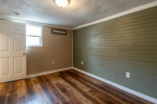 unfurnished room featuring baseboards, dark wood-style flooring, wood walls, and a textured ceiling