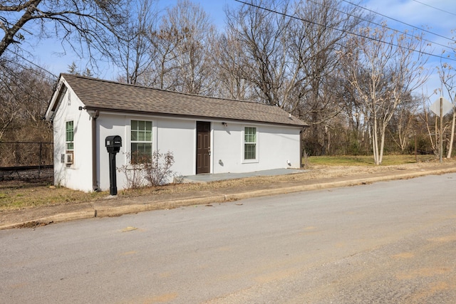 view of front of property featuring a shingled roof, fence, and stucco siding