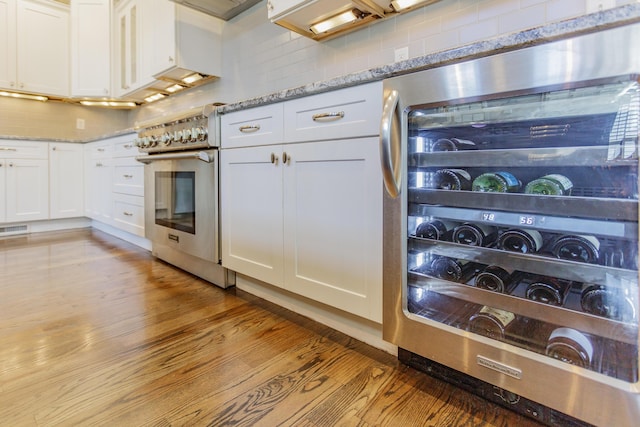 kitchen featuring beverage cooler, high end stainless steel range, light stone counters, tasteful backsplash, and white cabinets