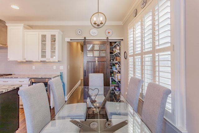 dining room featuring wood finished floors, a barn door, crown molding, baseboards, and a chandelier