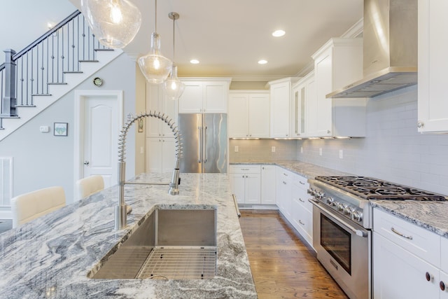 kitchen featuring pendant lighting, wall chimney exhaust hood, wood finished floors, high end appliances, and a sink