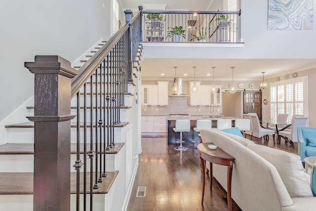 living area featuring visible vents, crown molding, dark wood-type flooring, stairs, and a high ceiling