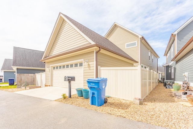 view of side of home with an attached garage, fence, driveway, and roof with shingles