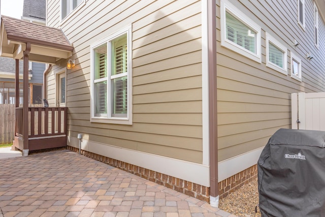 view of side of home with fence, a shingled roof, and a patio area