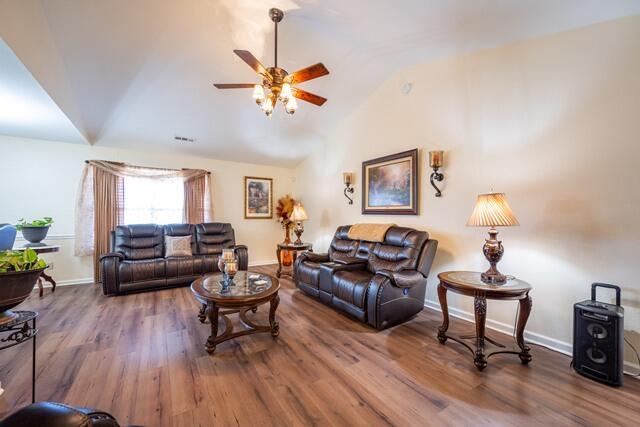 living room with ceiling fan, wood finished floors, baseboards, and vaulted ceiling