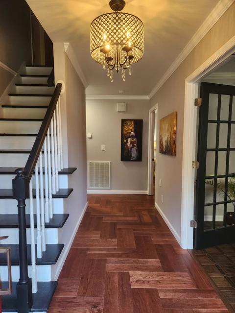 corridor with visible vents, baseboards, stairway, ornamental molding, and an inviting chandelier