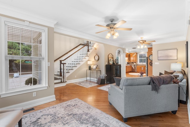 living room with stairs, visible vents, light wood finished floors, and ornamental molding