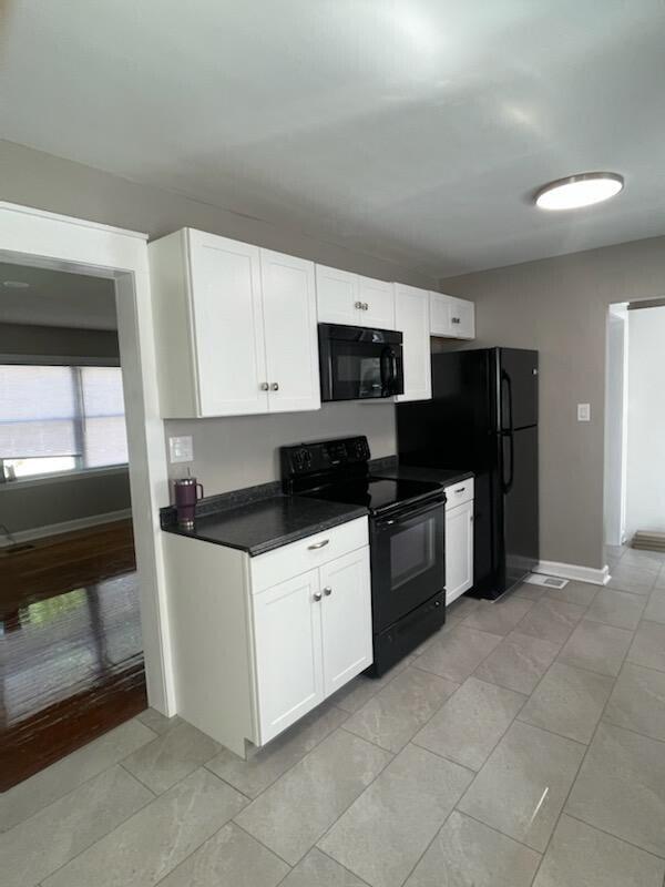 kitchen with baseboards, light tile patterned flooring, black appliances, white cabinets, and dark countertops