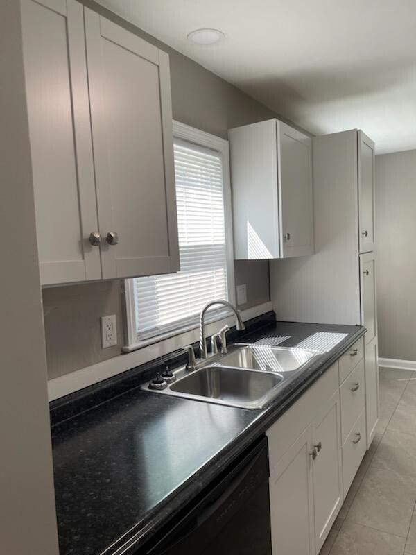 kitchen with dark countertops, baseboards, light tile patterned floors, white cabinets, and a sink