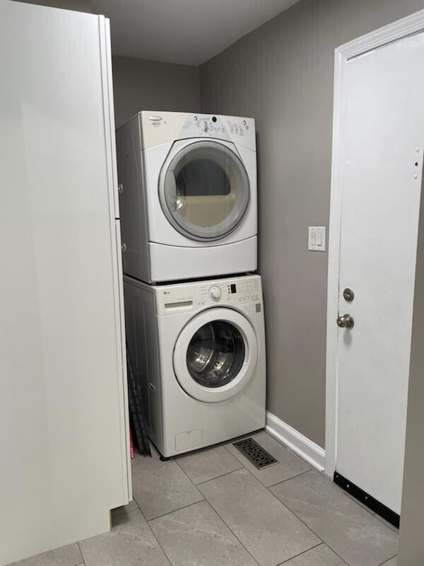 laundry area featuring light tile patterned floors, stacked washer / drying machine, baseboards, and laundry area