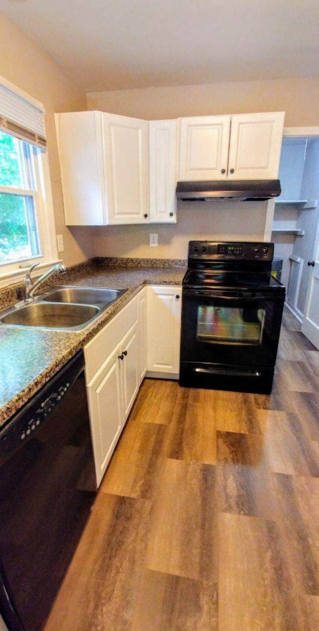 kitchen featuring wood finished floors, a sink, black appliances, under cabinet range hood, and white cabinetry